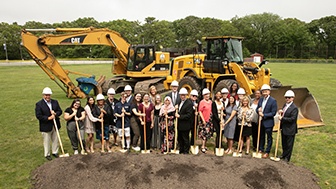 SJC students and staff and community members holding golden shovels towards the ground with a tractor behind them in the field where new student center will be built.